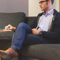 man sitting on a couch while using a laptop
